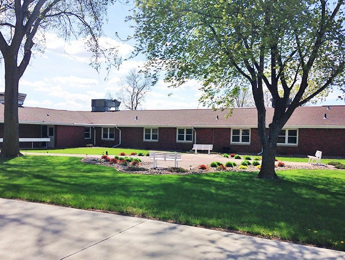 A brick building with a courtyard surrounded by trees and grass under a clear sky.