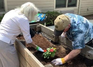 Two people working together to plant flowers in a raised garden bed.