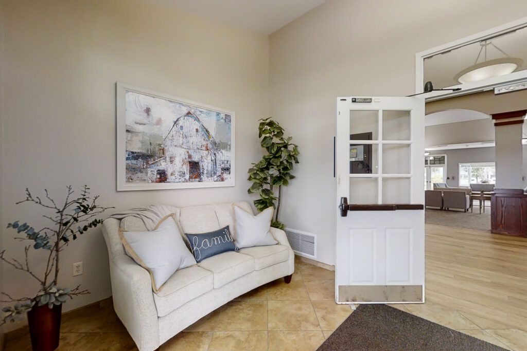 A cozy living room featuring a white sofa, an artwork on the wall, and a potted plant beside an open door.