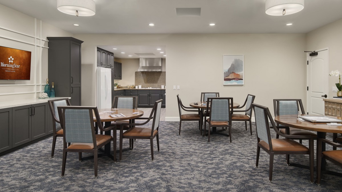 A well-appointed dining area with round tables and chairs, adjacent to a kitchen space.