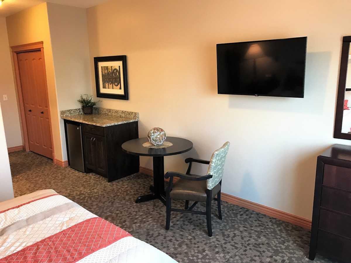 A modern hotel room featuring a flat-screen TV, a small table with a chair, and a neatly made bed.
