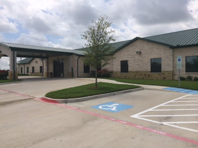 A brick building with a covered entrance and handicap parking spaces in the foreground, set under a cloudy sky.