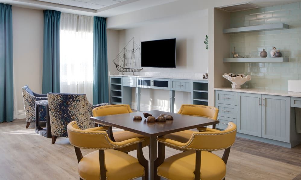 A modern living room with a dining table and yellow chairs, featuring a mounted television and stylish shelving.