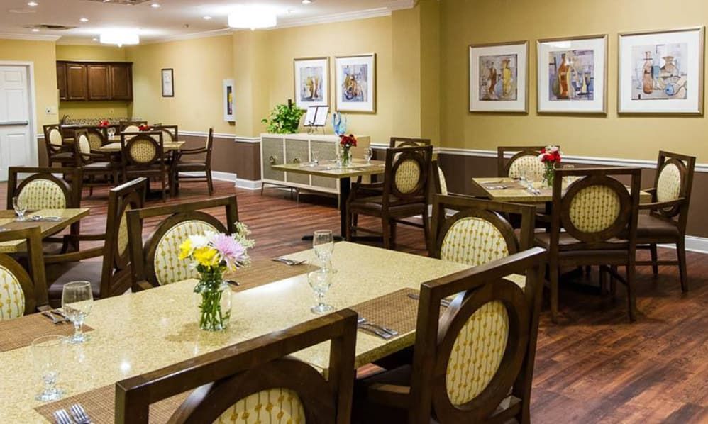 A well-decorated dining room with neatly arranged tables and chairs, adorned with flowers and paintings on the walls.