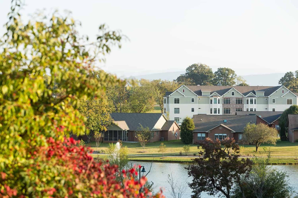 A scenic view of buildings by a lake surrounded by autumn trees.