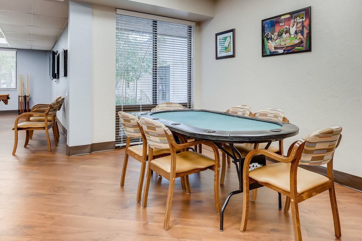 A room with a poker table and chairs, featuring hardwood floors and artwork on the walls.