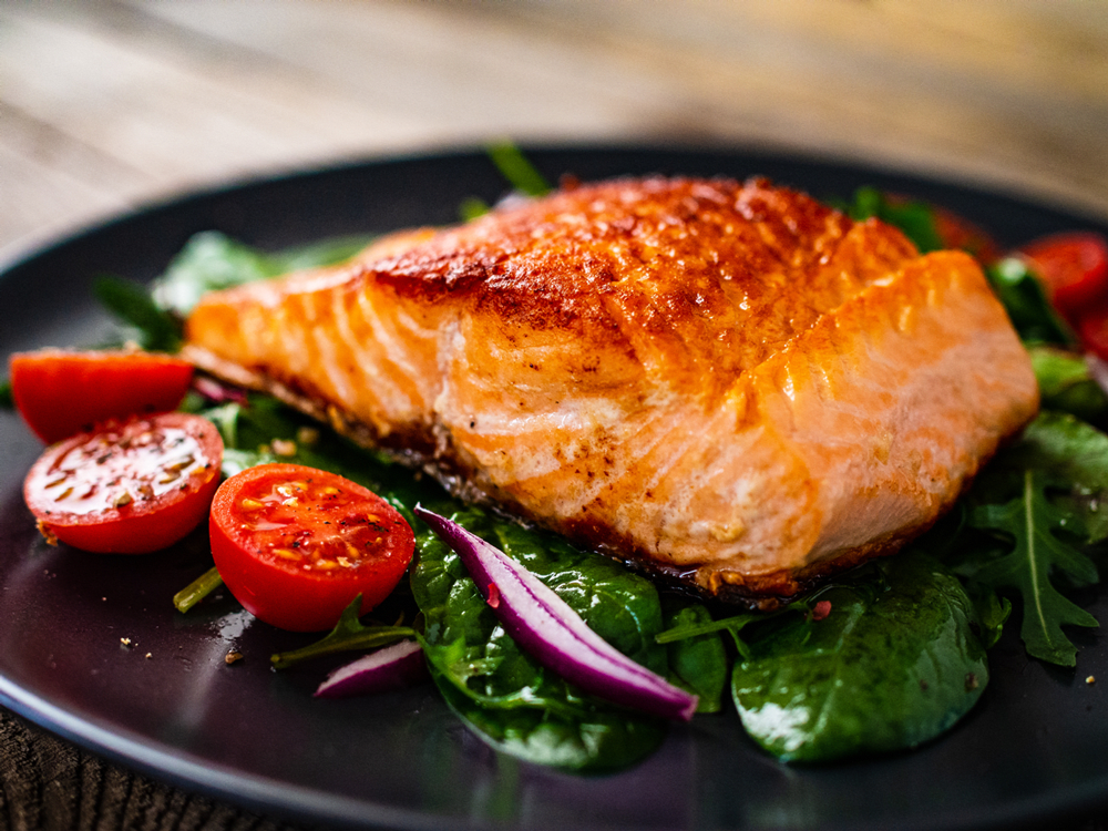 A delicious grilled salmon fillet served on a bed of spinach with roasted tomatoes and sliced onions.