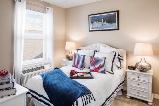 A cozy bedroom with a nautical theme, featuring a neatly made bed adorned with anchor-patterned pillows and a blue throw blanket.