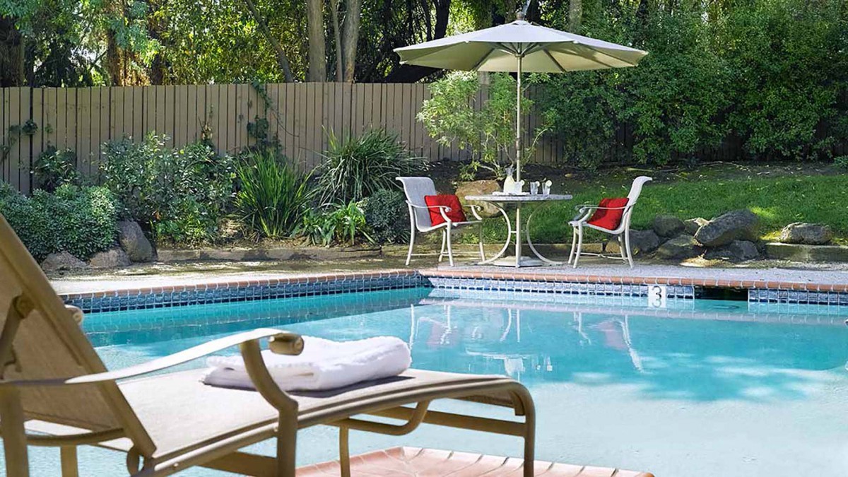 A serene backyard setting featuring a swimming pool with lounge chairs and patio furniture under an umbrella.