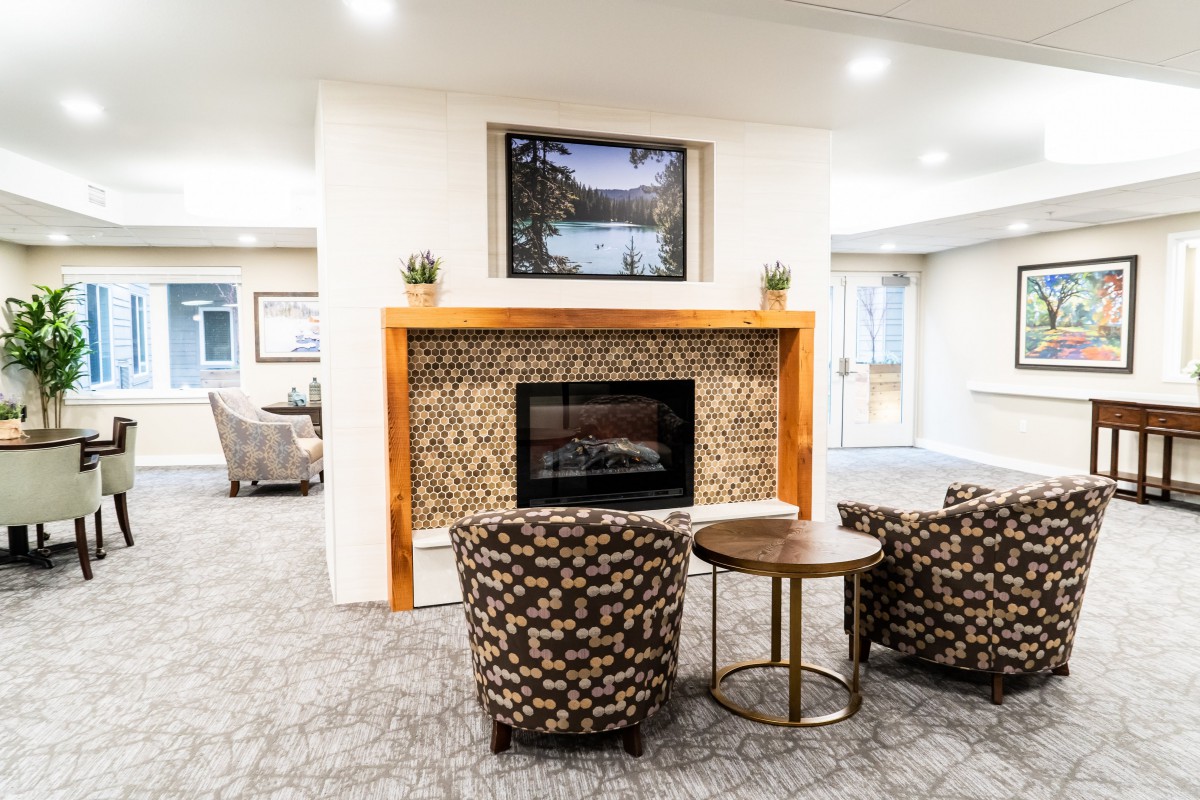 A cozy living room with a modern fireplace, flanked by two patterned armchairs and a small coffee table.