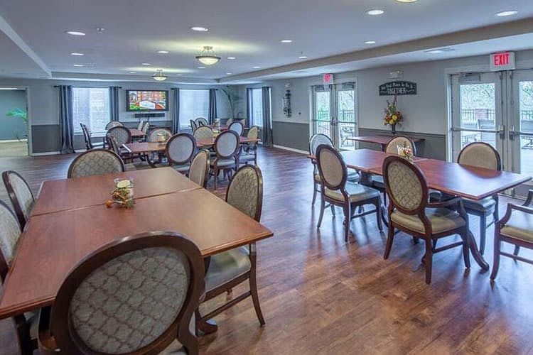 A spacious dining room with multiple tables and chairs, featuring a wooden floor and a chandelier.