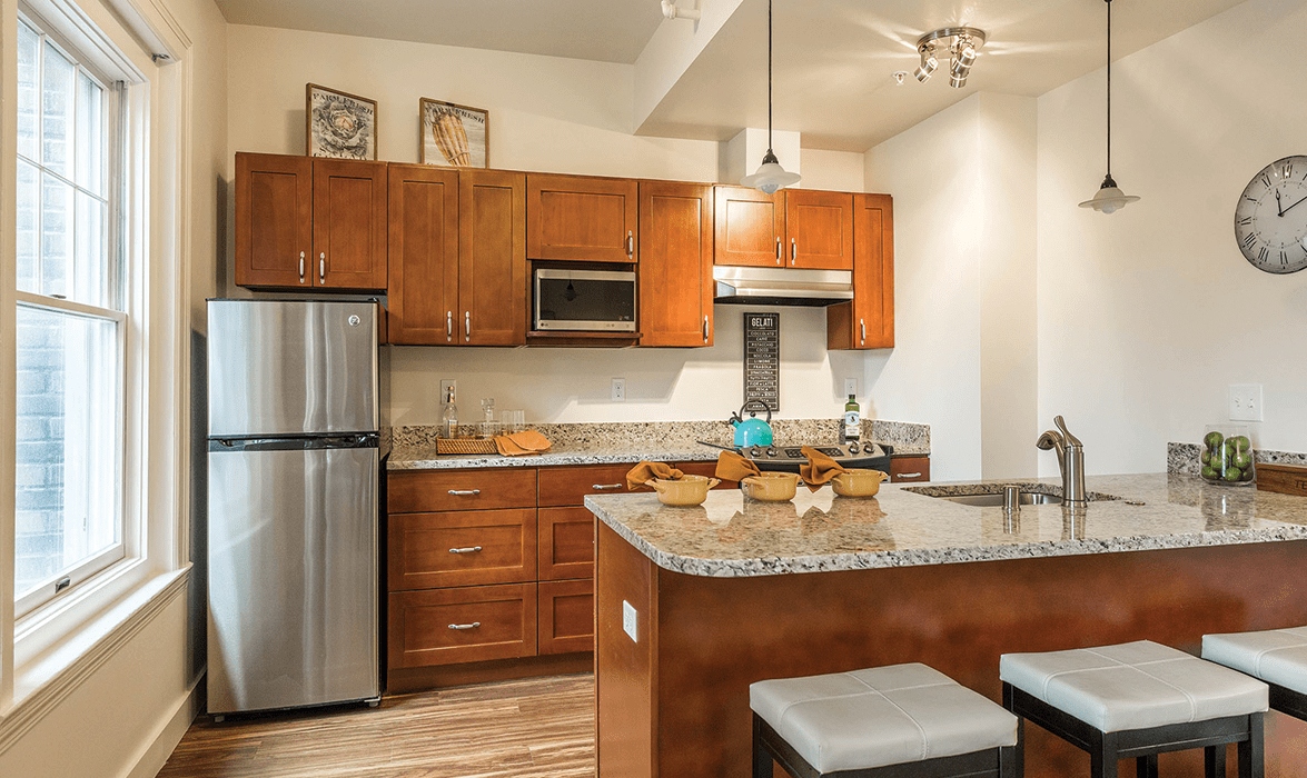 A modern kitchen with wooden cabinets, stainless steel appliances, and a central island with stools.