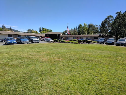 A wide view of a grassy area in front of a building with several parked cars under a clear blue sky.
