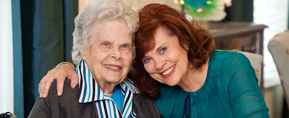An elderly woman and a middle-aged woman smiling together in a close-up portrait.