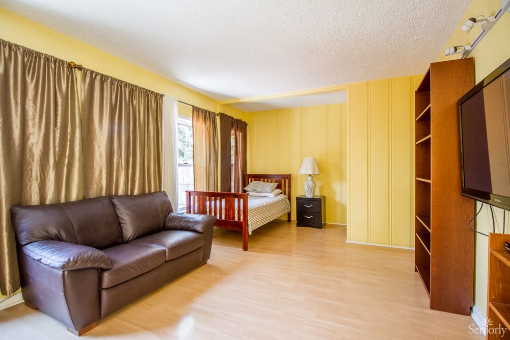 A spacious bedroom with yellow walls, featuring a bed, sofa, and wooden flooring.
