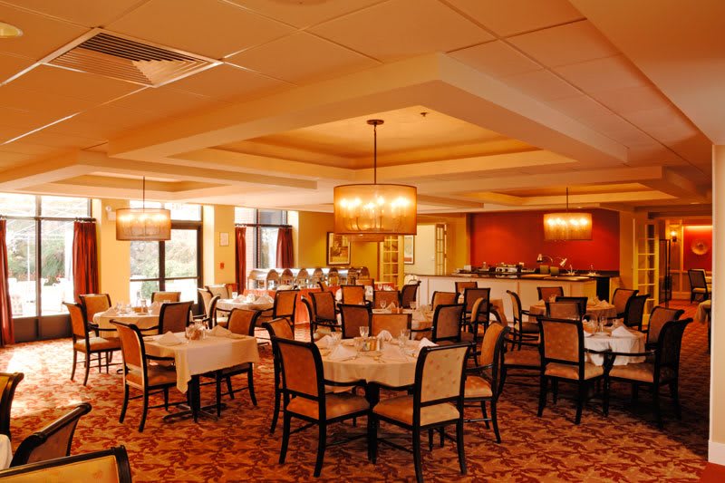A spacious and elegant restaurant dining room with neatly arranged tables and chairs, illuminated by warm chandeliers.