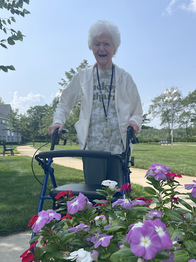 An elderly woman enjoying a sunny day in the park, surrounded by colorful flowers.