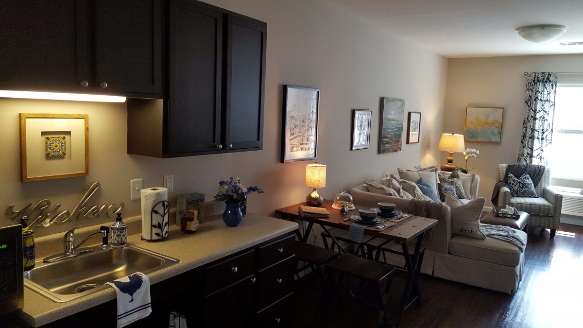 A cozy living space featuring a small dining area and kitchenette, adorned with artwork and soft lighting.