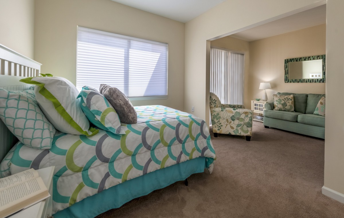 A cozy bedroom with a colorful bedspread, pillows, and an adjoining sitting area.