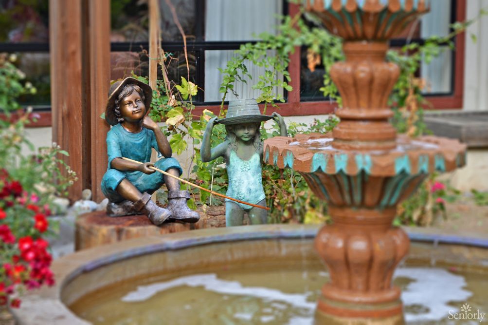 Garden scene with decorative statues of children near a fountain.