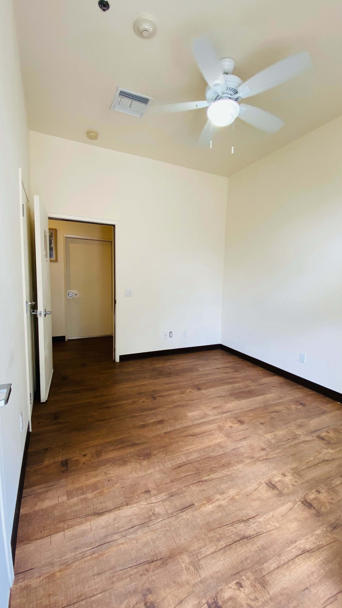 An empty room with wooden flooring and white walls, featuring an open door leading to another space.