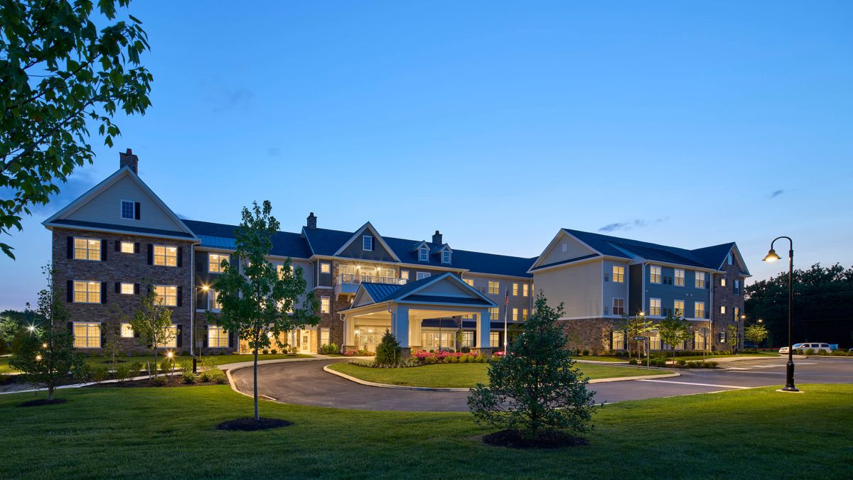A well-lit hotel building at night with neatly landscaped surroundings.