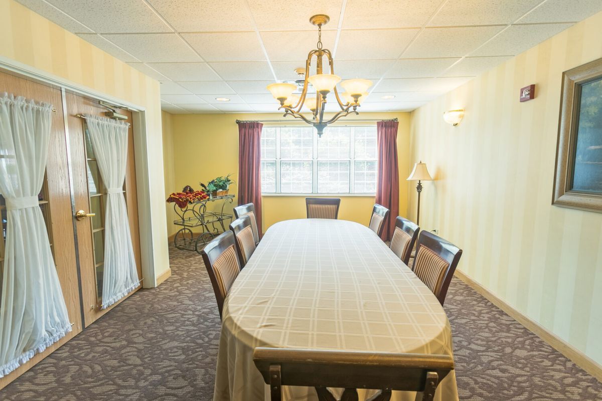 A bright dining room with a long table, surrounded by chairs and illuminated by a chandelier.