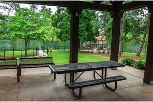 A peaceful park area with a picnic table and benches under a shelter surrounded by lush greenery.