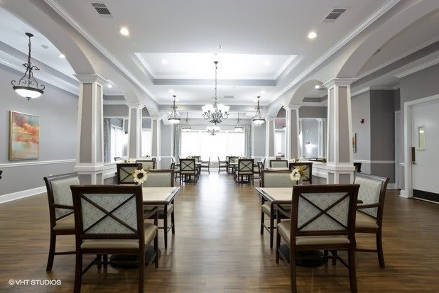 A spacious and elegantly designed dining room with chandeliers, columns, and neatly arranged tables and chairs.