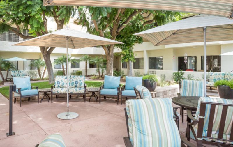 A serene outdoor patio area with comfortable seating and umbrellas, surrounded by lush greenery.