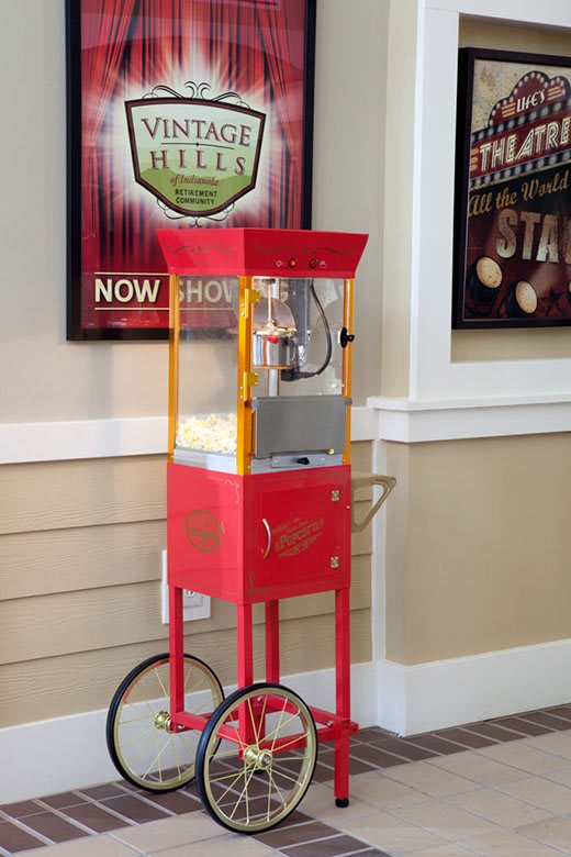 A vintage red popcorn machine with wheels stands indoors against a wall adorned with movie posters.