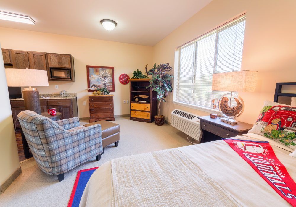 A cozy bedroom with a large window, comfortable chair, and warm lighting.