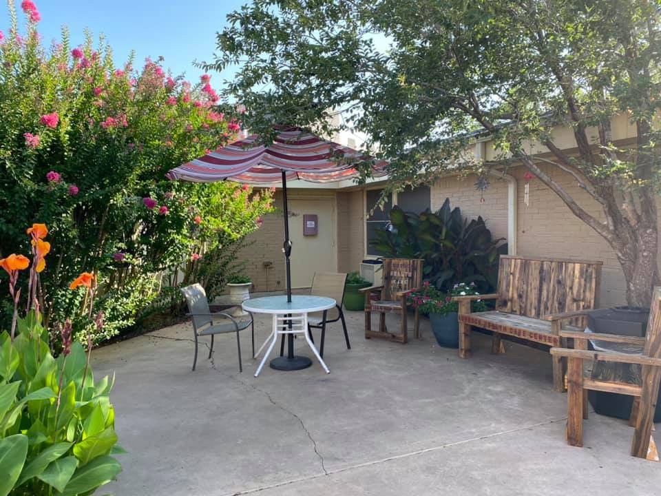 A cozy patio with a table and chairs under an umbrella, surrounded by lush greenery.