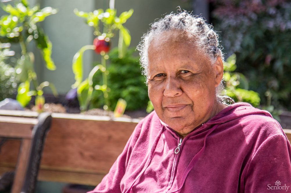 An elderly woman sitting outside in a garden on a sunny day.