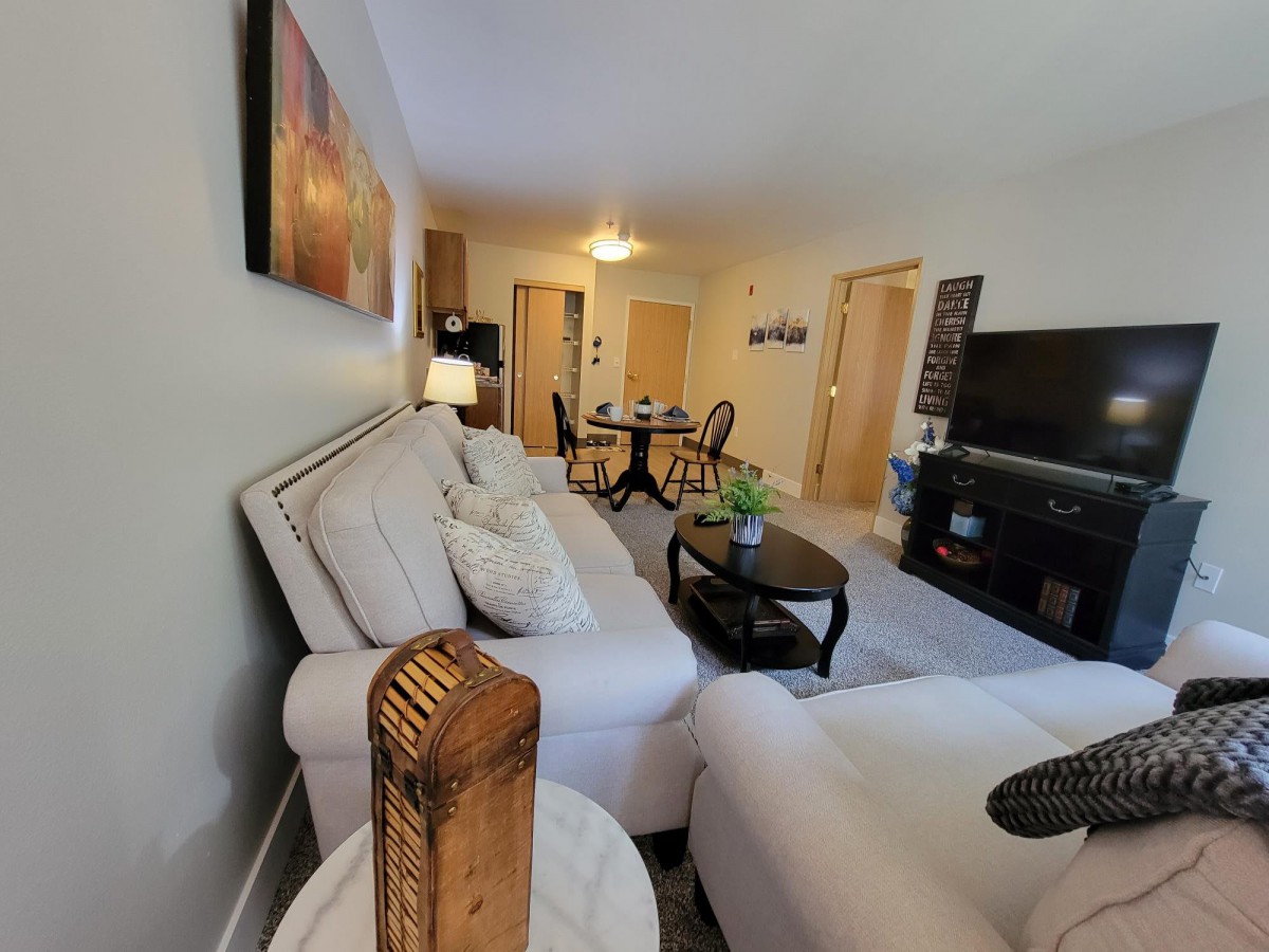 A cozy living room featuring a white sofa, coffee table, and television, with a dining area in the background.