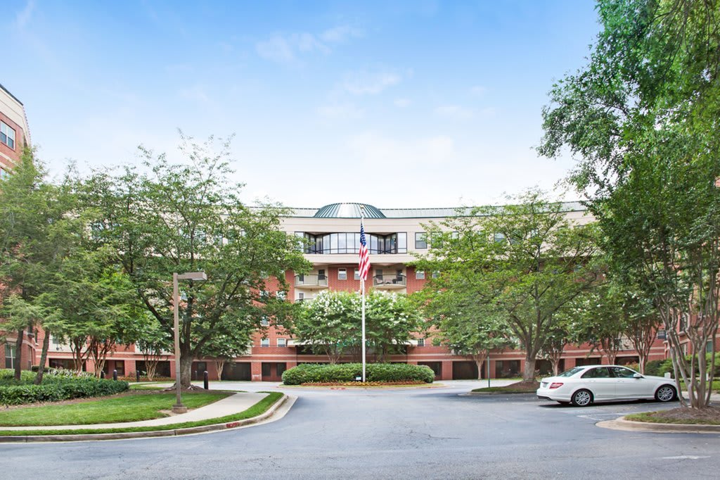 A view of an office building surrounded by trees and a parking lot, featuring a flagpole at the entrance.
