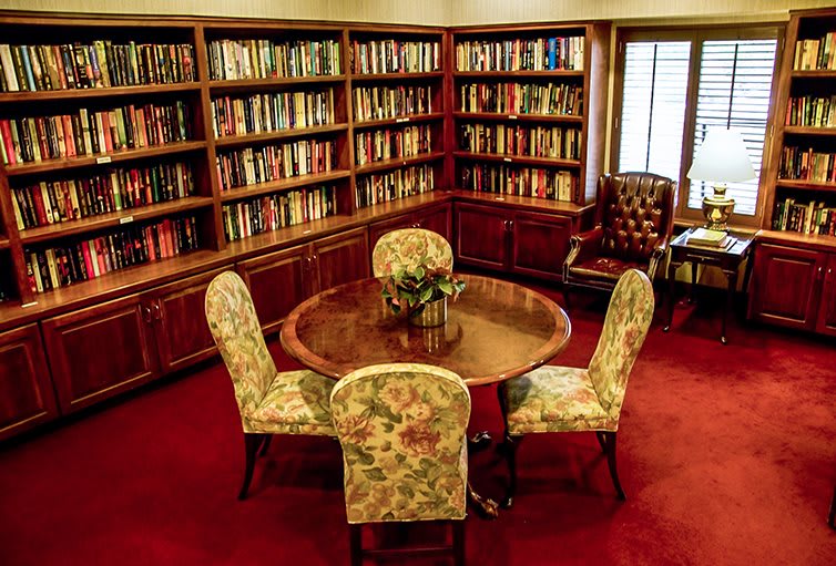 A cozy library room with wooden bookshelves, a round table, and upholstered chairs.