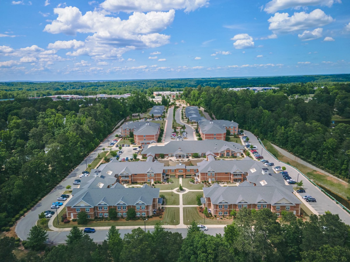 Aerial view of a large apartment complex surrounded by trees under a partly cloudy sky.
