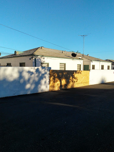 A residential building surrounded by a white fence, illuminated by sunlight in an urban setting.