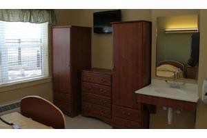A room featuring wooden wardrobes, a dresser, a wall-mounted television, and a mirror.