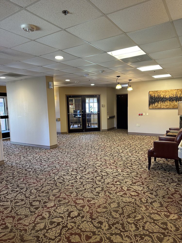 A neatly arranged lobby area featuring chairs, patterned carpet, artwork on the wall, and ceiling lights.