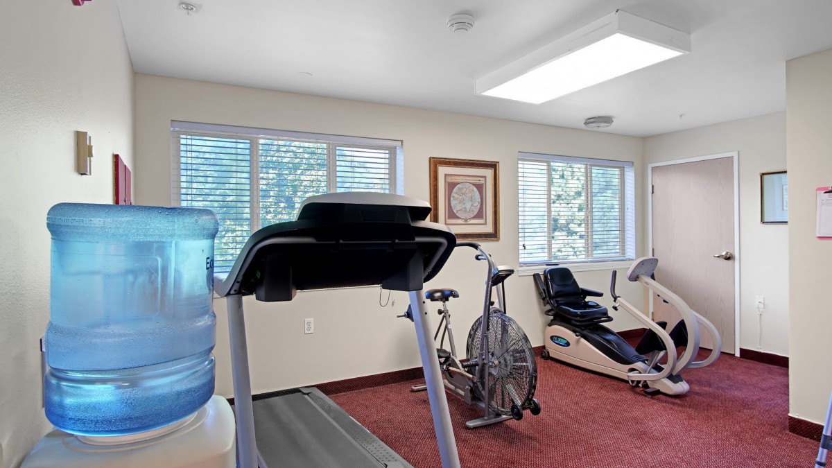 A well-lit gym with various exercise equipment including a treadmill and stationary bike.