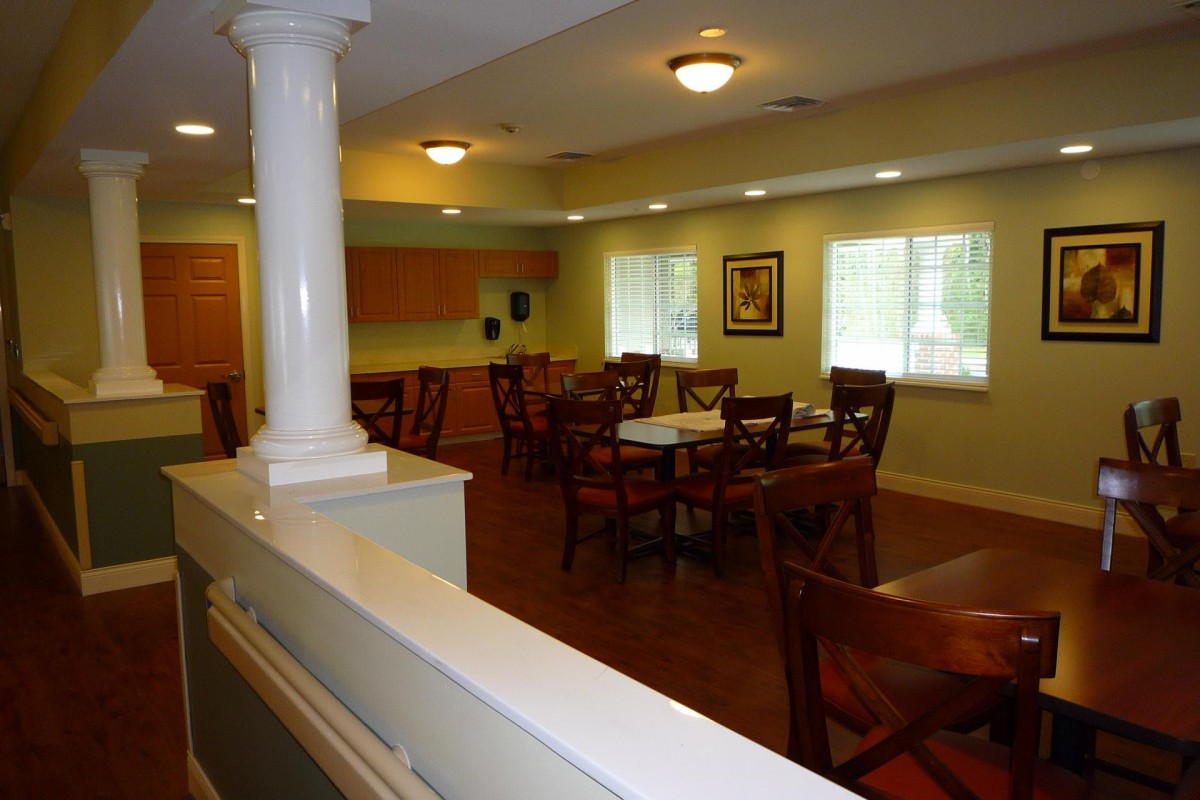 A cozy dining room with several tables and chairs, illuminated by overhead lights, featuring large windows and a warm atmosphere.