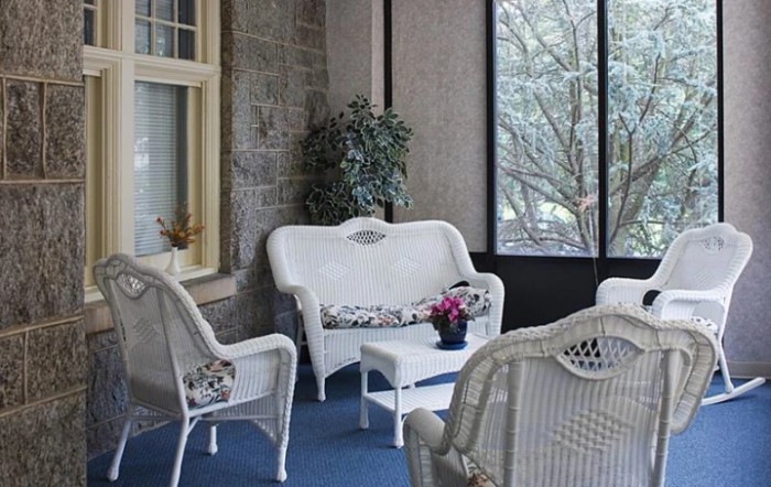 A cozy indoor patio area featuring white wicker furniture and a potted plant.