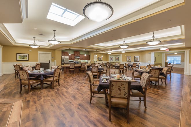 A spacious and elegantly designed dining area with neatly arranged tables and chairs, featuring warm lighting and a wooden floor.