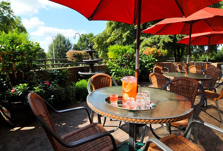 A sunny outdoor patio with a table set for refreshments under a red umbrella.