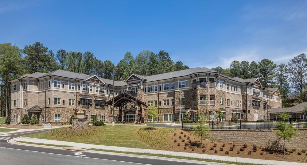 A modern residential building surrounded by landscaped greenery and trees under a clear blue sky.