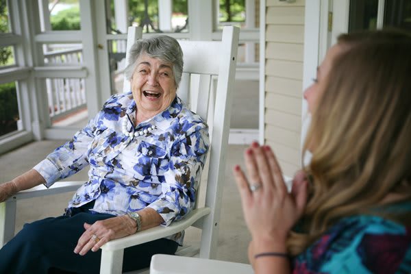 An elderly woman laughing and enjoying a conversation on a porch.