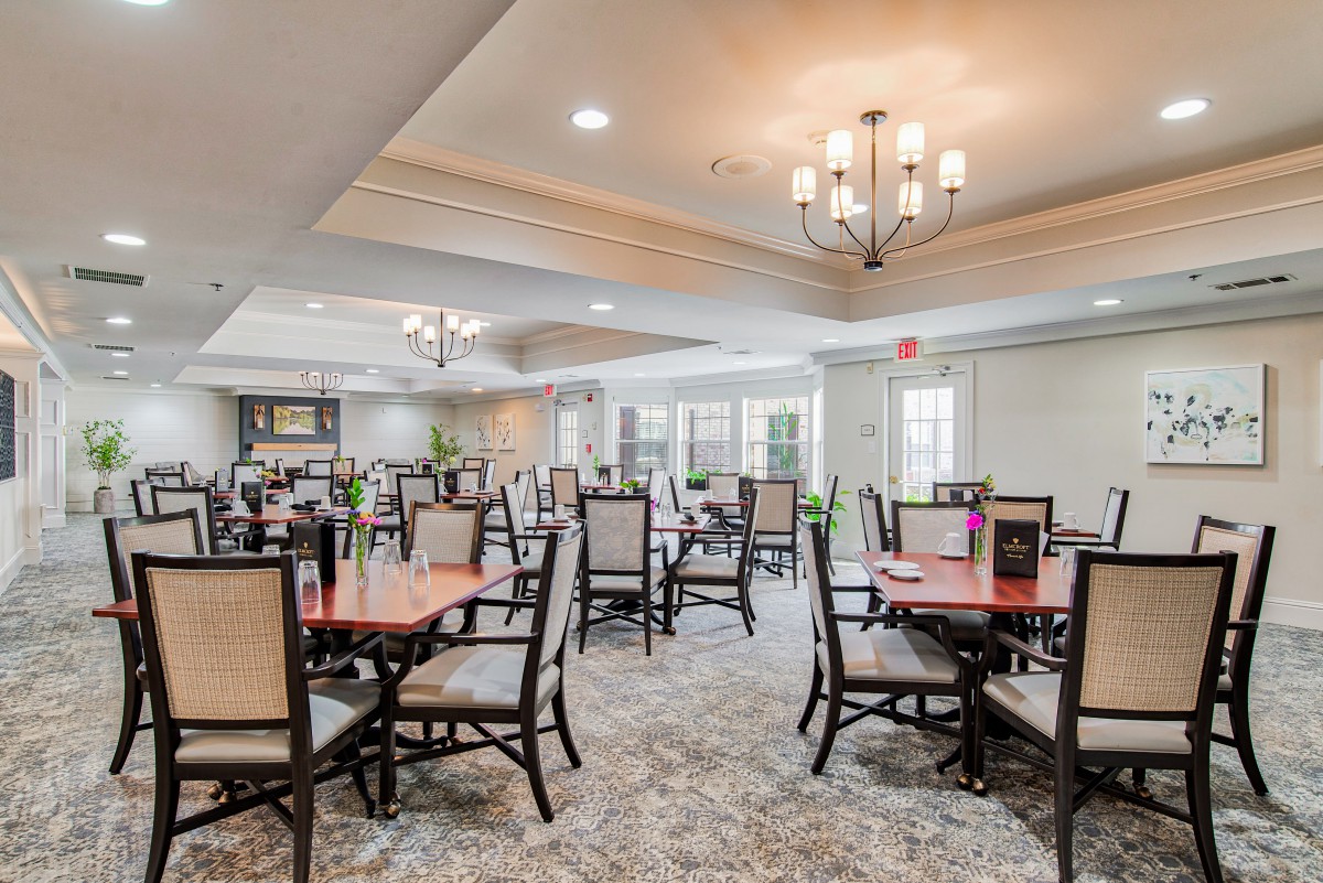 A spacious dining area with elegantly set tables and comfortable seating, illuminated by chandeliers.