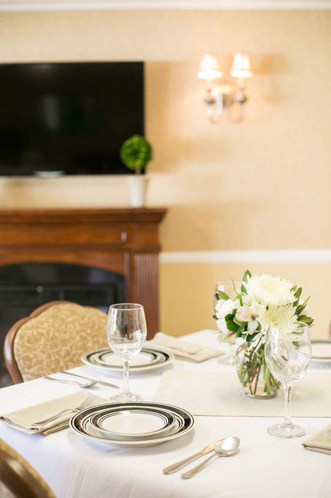 An elegantly set dining table with floral centerpiece and glassware, positioned in a cozy room with a fireplace.